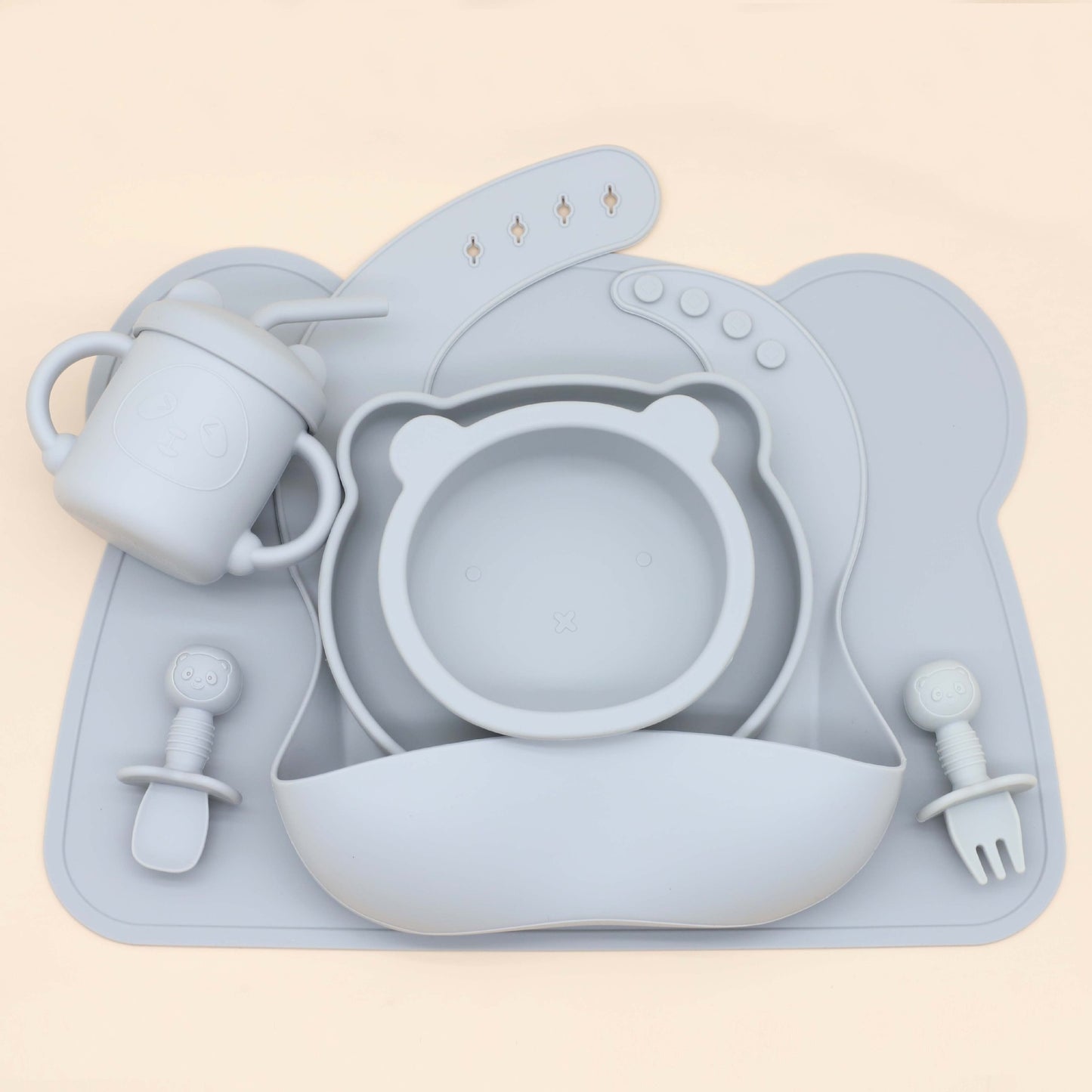 סט כלי אוכל לתינוקות בצבע כחול הכולל סינר, כוס שתייה עם ידיות, קערת אוכל בצורת ראש דב, וכפית ומזלג לתינוקות, עשוי מסיליקון רך ונוח לשימוש